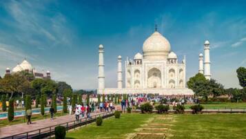 El Taj Mahal bajo un cielo despejado, un amplio césped y visitantes alrededor.