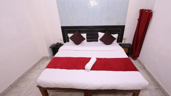 A neatly made bed with a red and white bedspread, a wooden headboard, and a nightstand with a lamp. - Hotel NoVo Agra (Agra)