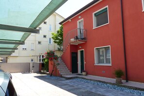 Un bâtiment rouge doté d’un balcon, d’un escalier et d’un petit jardin agrémenté de fleurs.