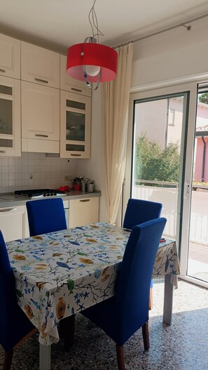 Un coin repas avec une table dressée pour quatre personnes, un luminaire suspendu rouge et une vue sur l’extérieur grâce à une porte vitrée.