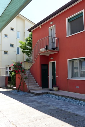 A two-story building with a red facade, a green door, and a small balcony. - Beautiful apartment in Jesolo, PVT parking (Città Metropolitana di Venezia)