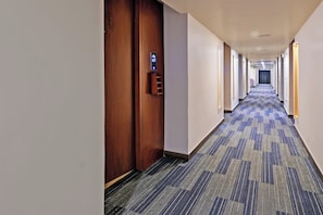 A hotel corridor with a carpeted floor, wooden doors, and a digital display on the wall.