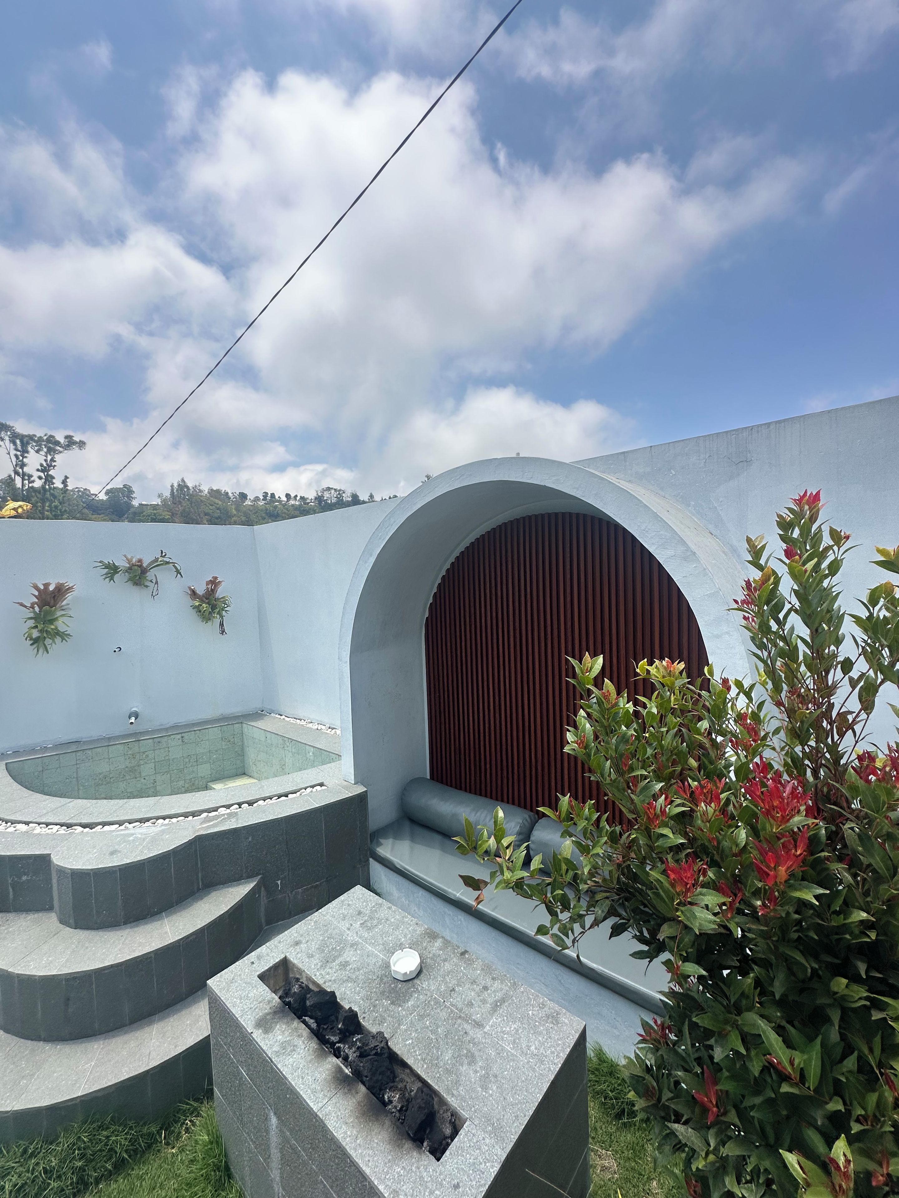 Un área de piscina moderna al aire libre con un jacuzzi integrado, asientos y una chimenea.