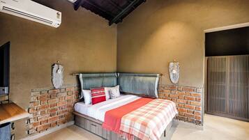 A bedroom with a brick wall, a bed with a checkered blanket, and a mounted TV.