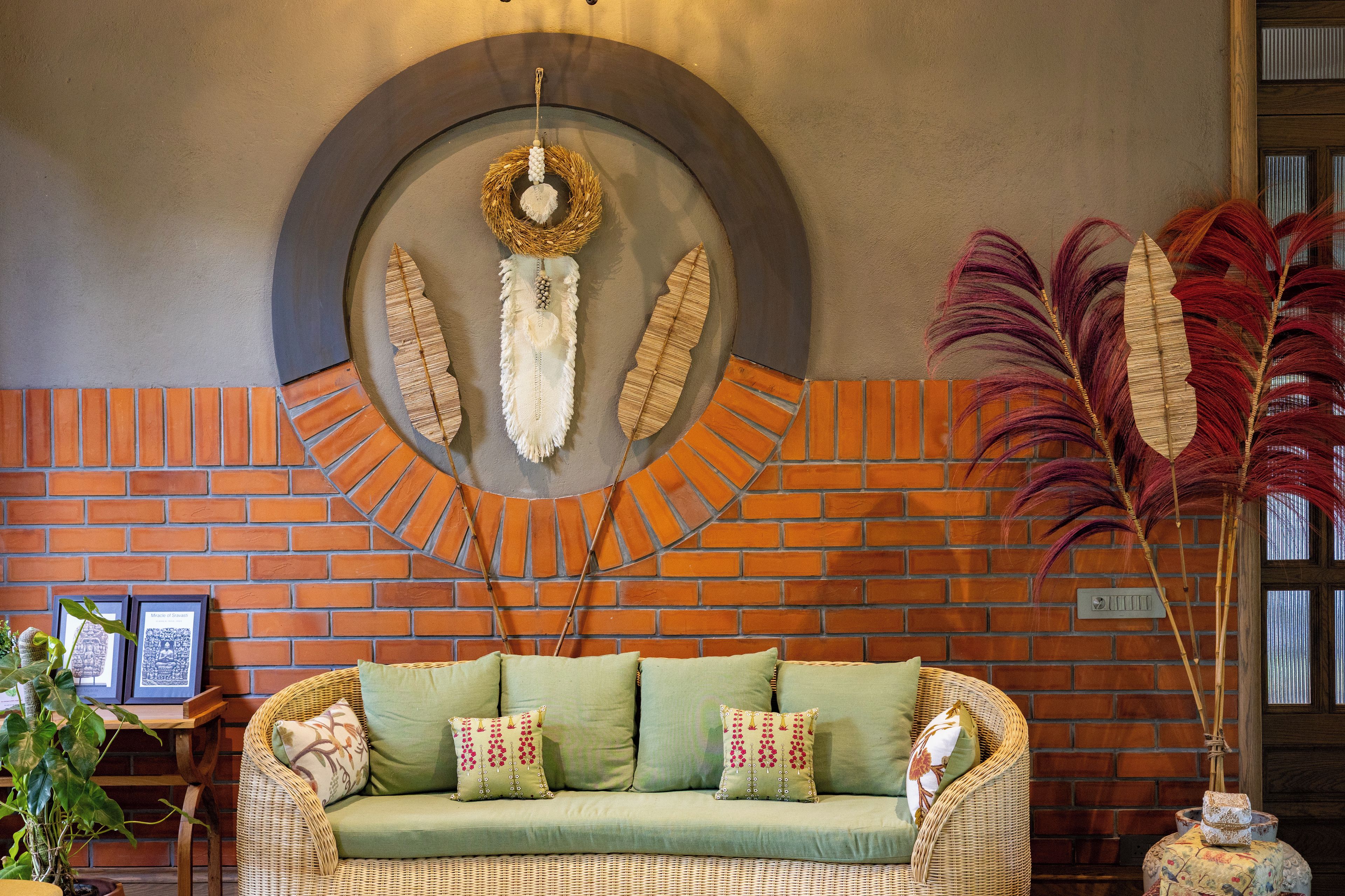 Una habitación con pared de ladrillo, un adorno circular en la pared, un sofá de mimbre con cojines y una planta en maceta.