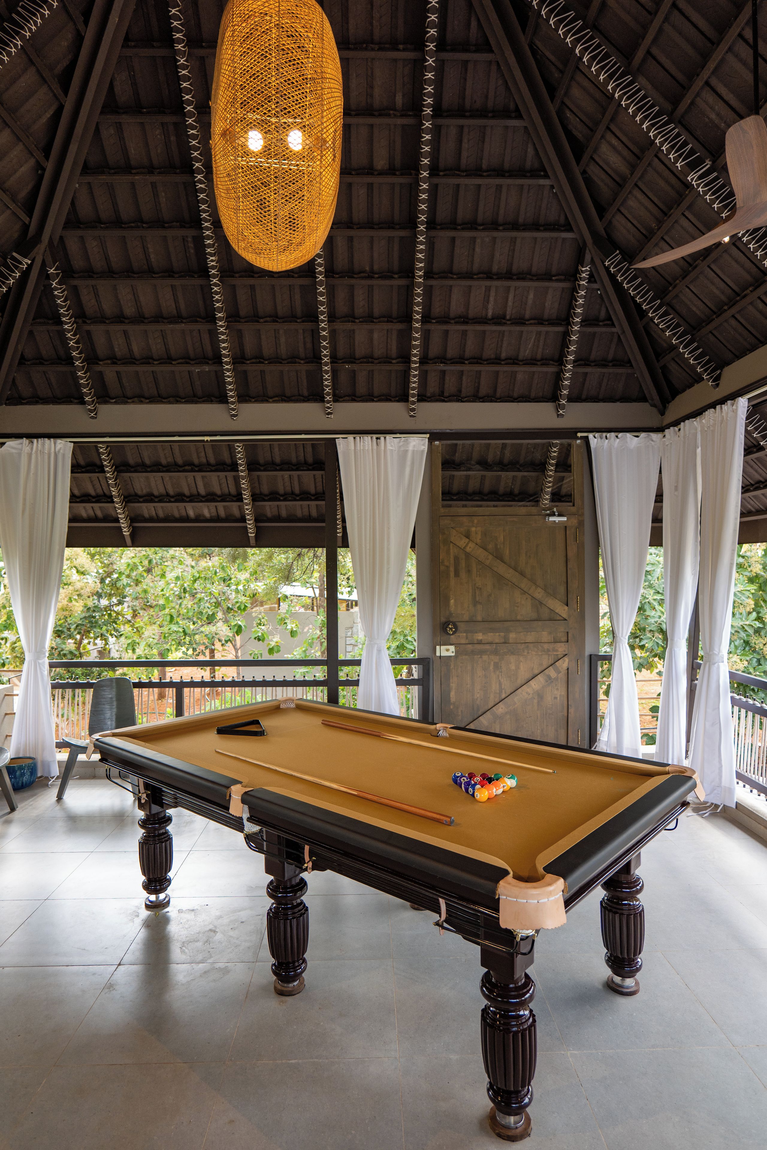 A pool table with balls, a hanging light fixture, and a view of greenery outside.