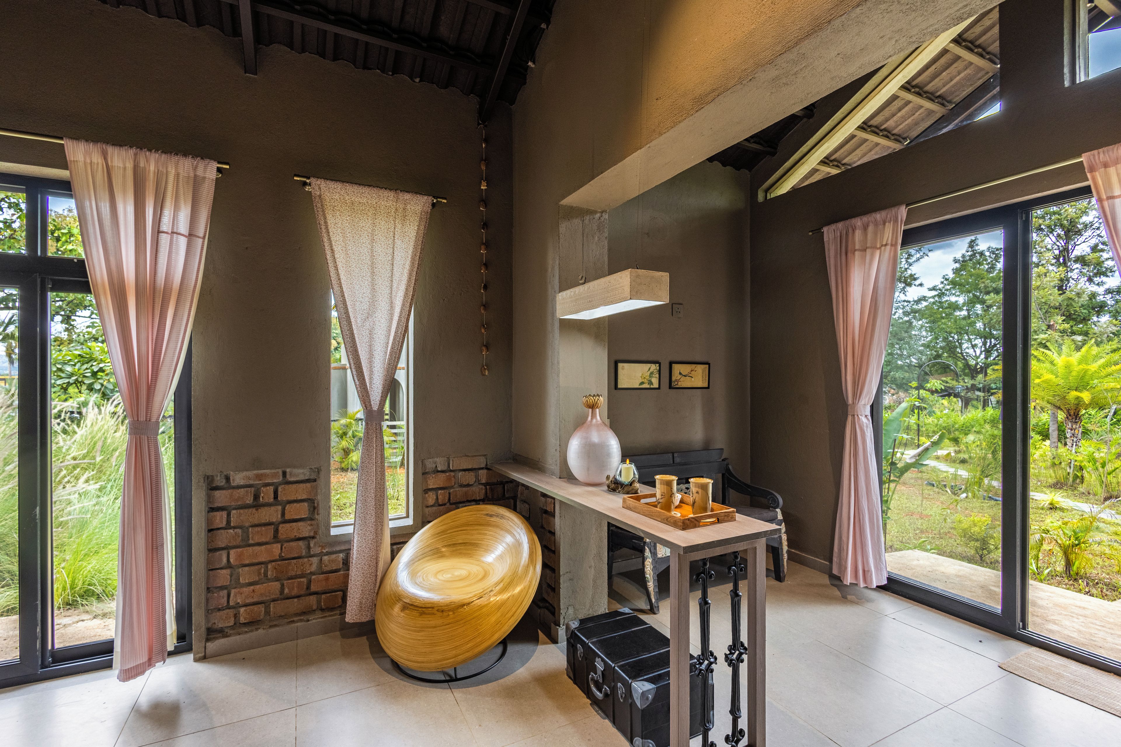 A room with large windows, a wooden chair, a table with a tray, and a brick wall.