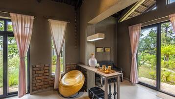 A room with large windows, a wooden chair, a table with a tray, and a brick wall.