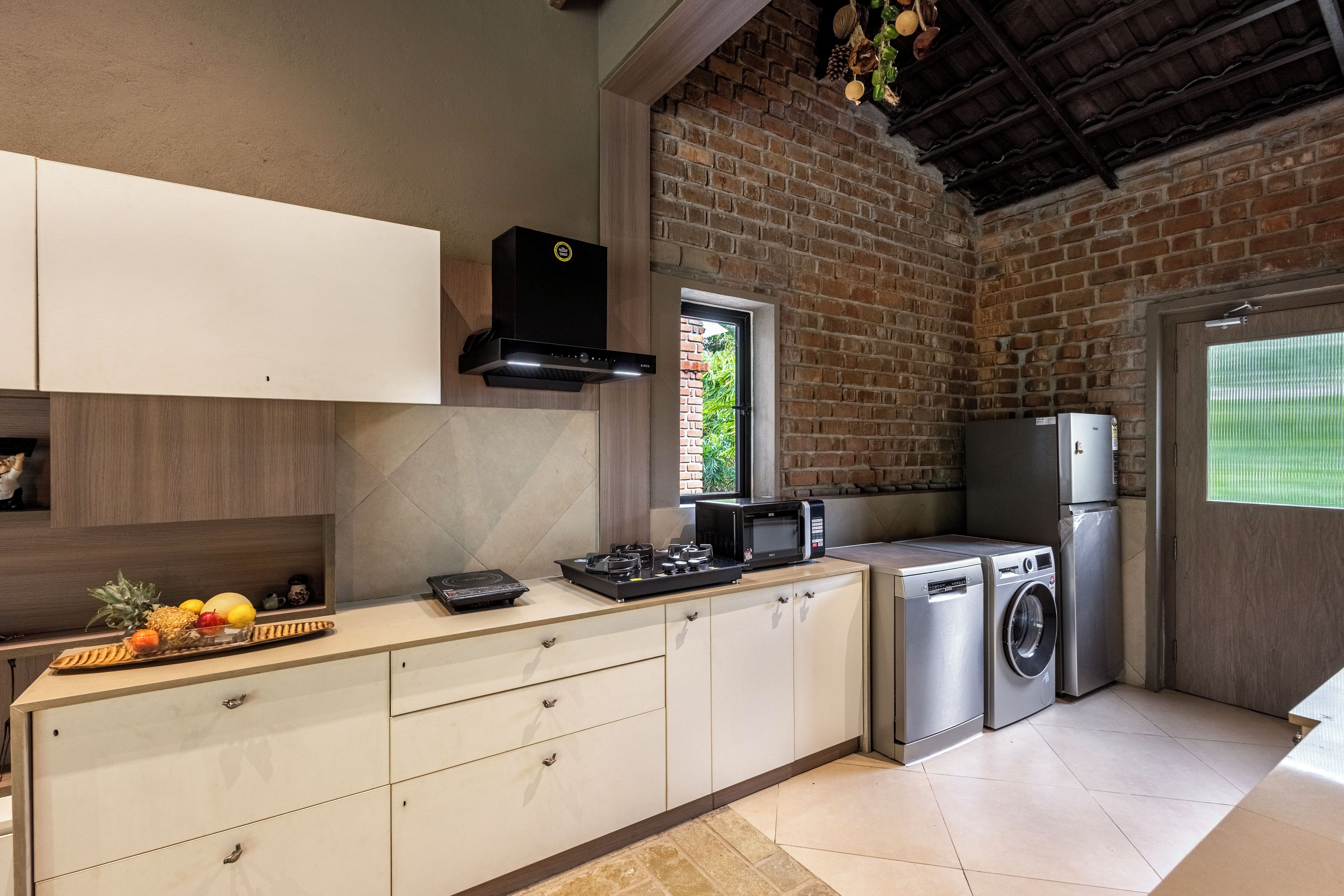 A modern kitchen with a brick wall, a built-in oven, a microwave, and a washing machine.