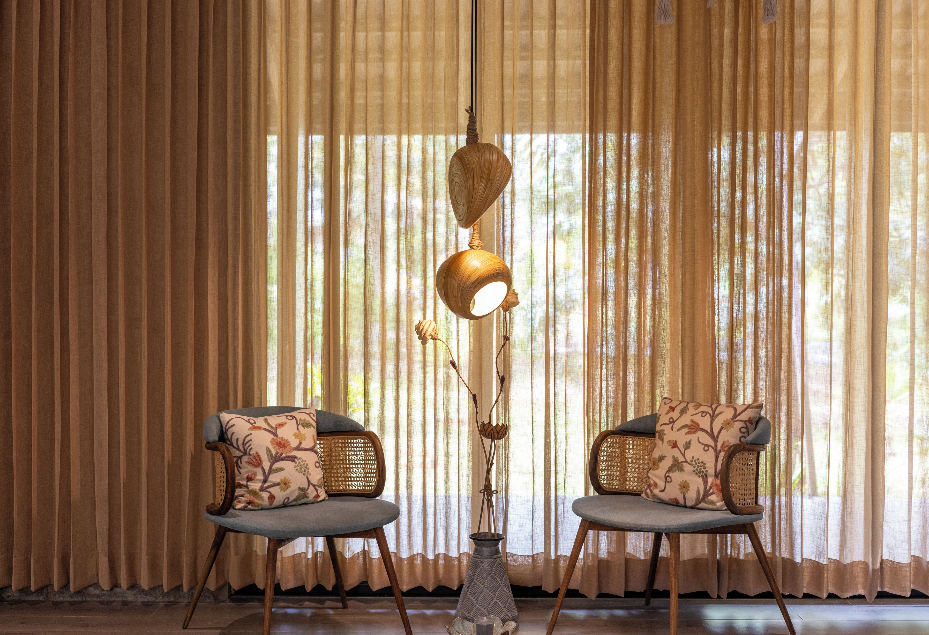 Una habitación con dos sillones de mimbre, una lámpara de pie y cortinas traslúcidas.