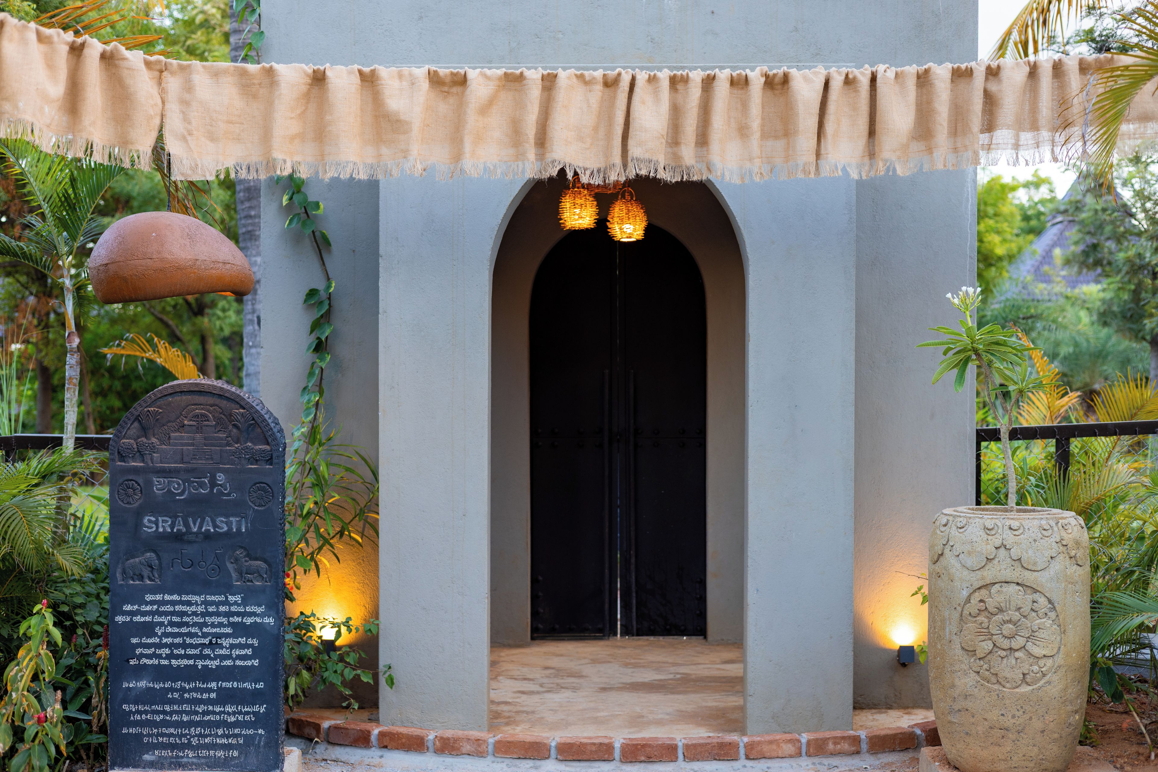 A building entrance with a covered archway, a stone plaque with inscriptions, and a potted plant.