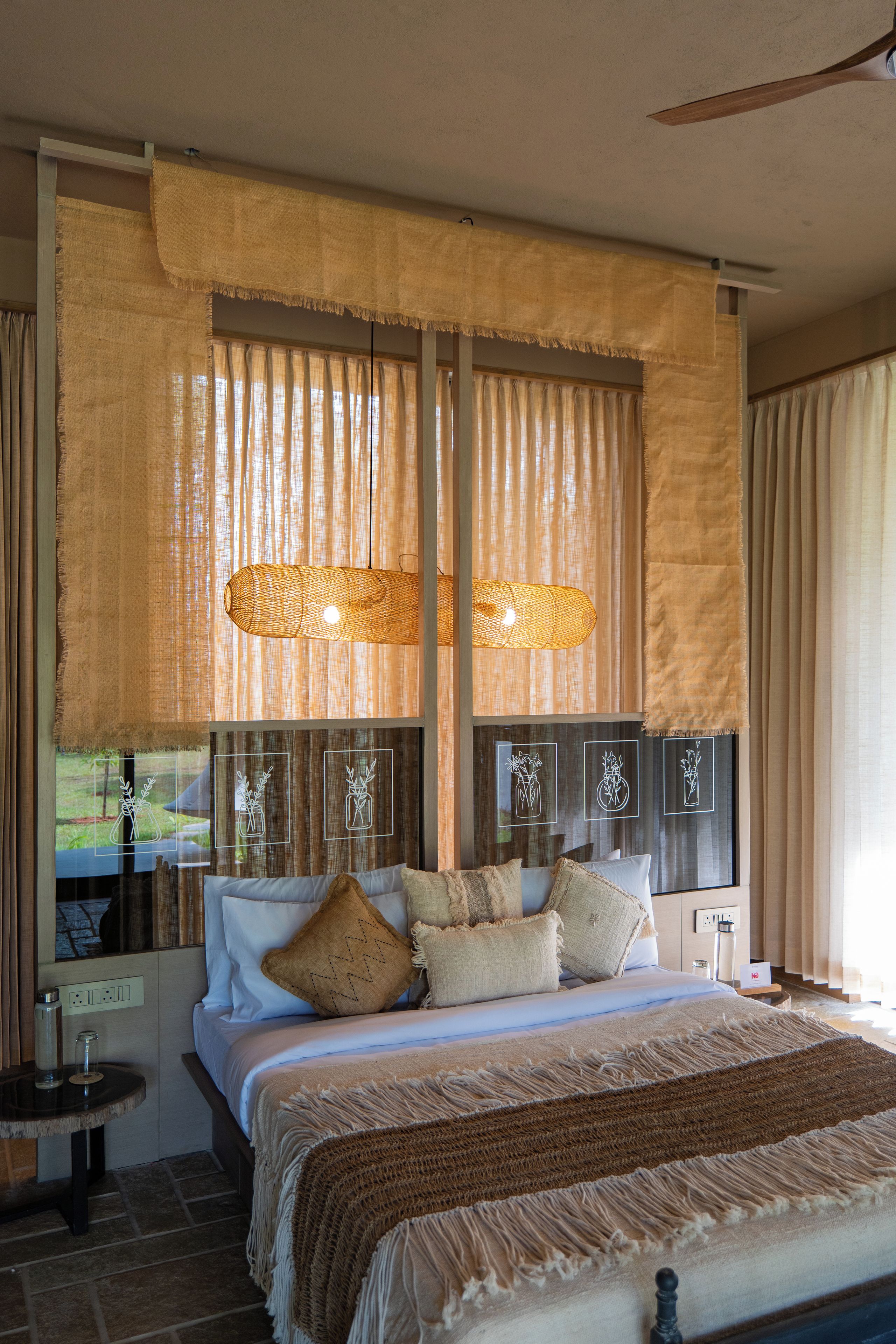 A bedroom with a large bed, multiple pillows, a bedside table, and a window with curtains.