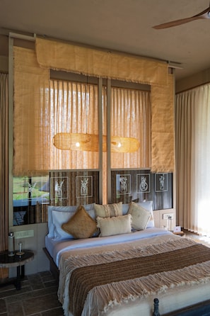 Un dormitorio con una cama grande, varias almohadas, una mesita de noche y una ventana con cortinas.
