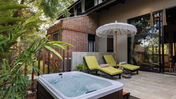 A spa area with a hot tub, lounge chairs, and a large umbrella.