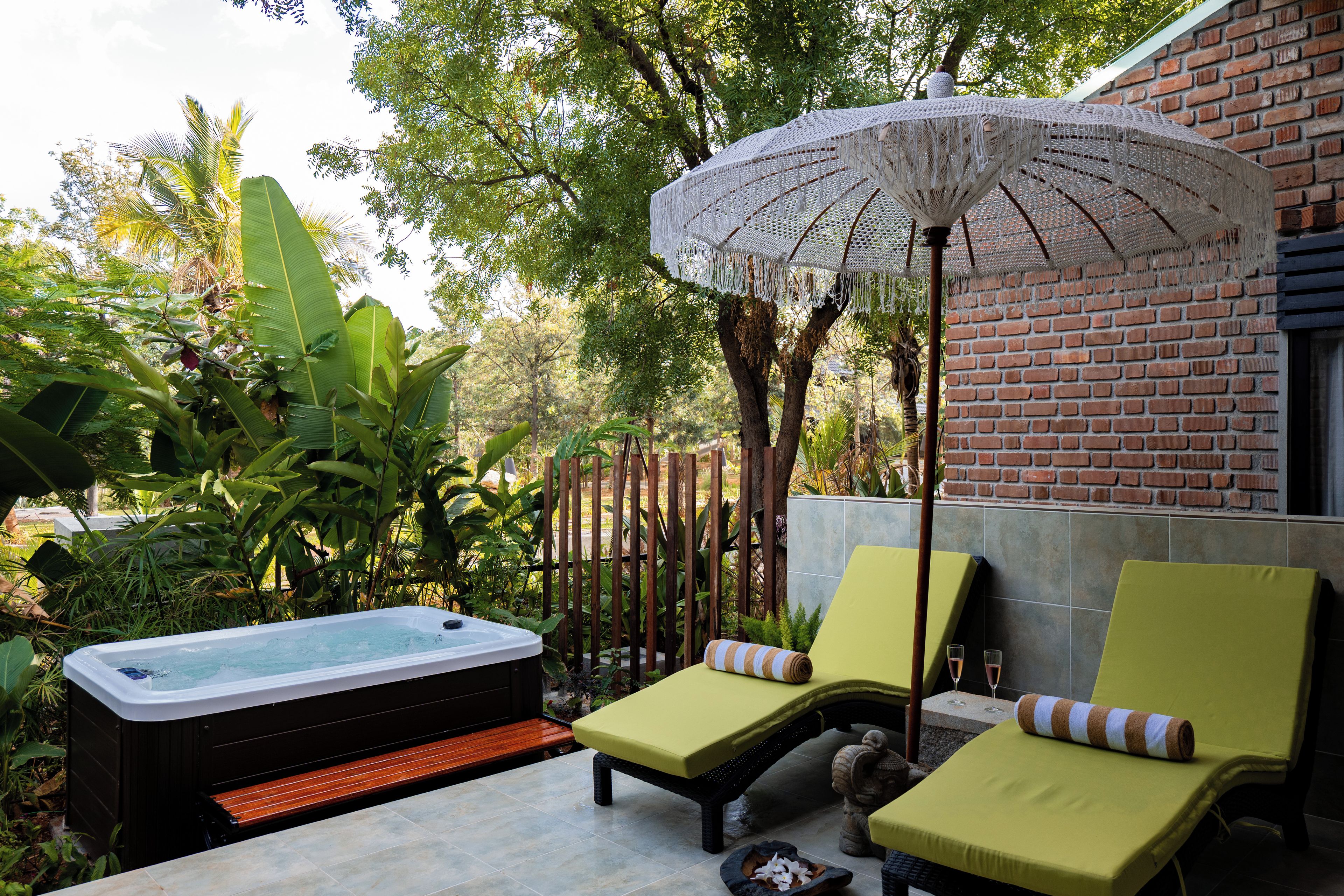 A hot tub, lounge chairs, and a large umbrella in a garden setting.