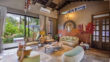 A spacious living area with a sofa, chairs, a coffee table, and a view of greenery through large windows.