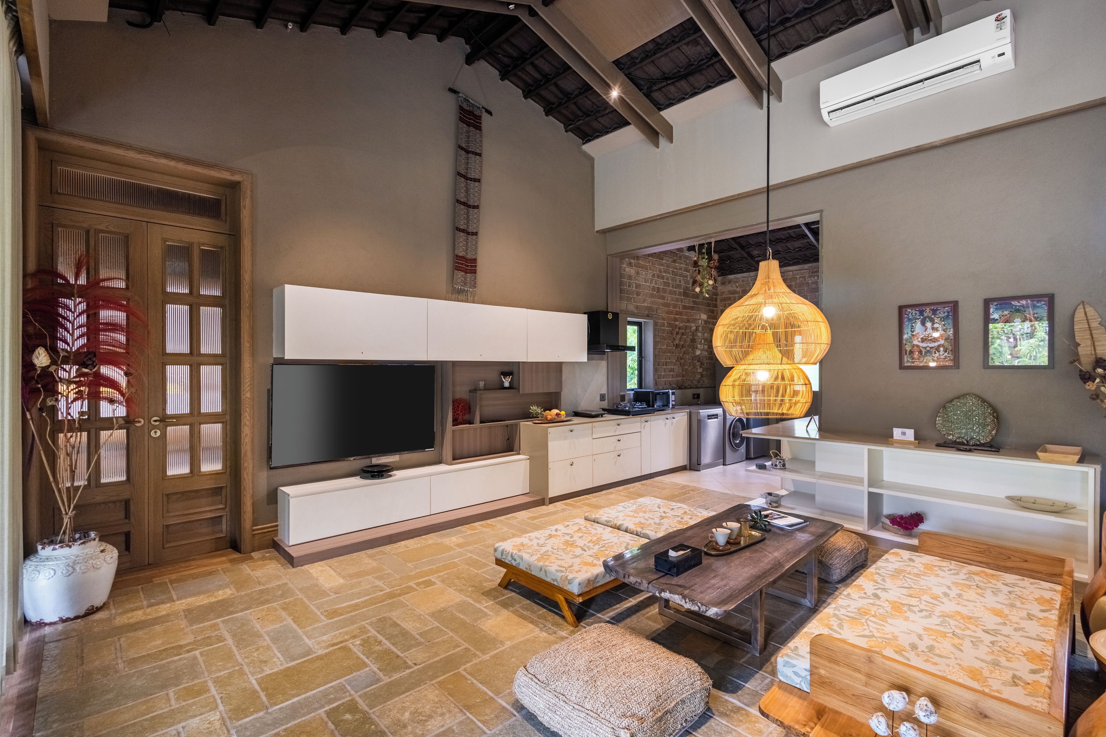 A modern living room with a flat-screen TV, a large woven light fixture, and a stone-tiled floor.