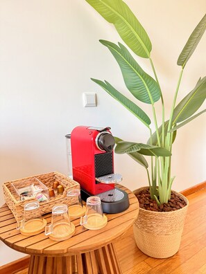 Una màquina de cafè vermella sobre una taula de fusta, amb una cistella teixida que conté tasses i una planta en test amunt.