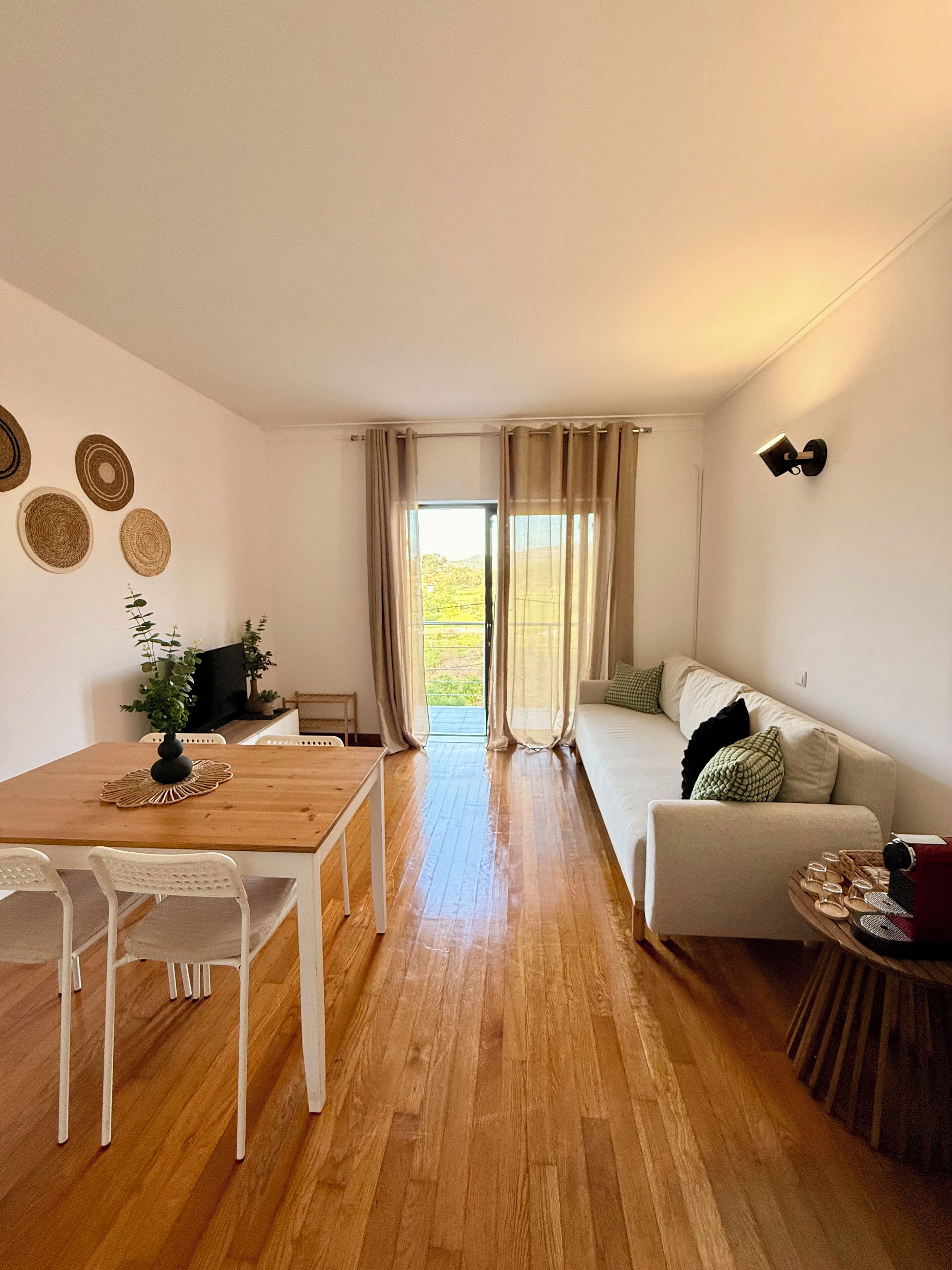 Une pièce avec un plancher en bois, un canapé, une table à manger avec des chaises, un téléviseur et une fenêtre avec des rideaux.