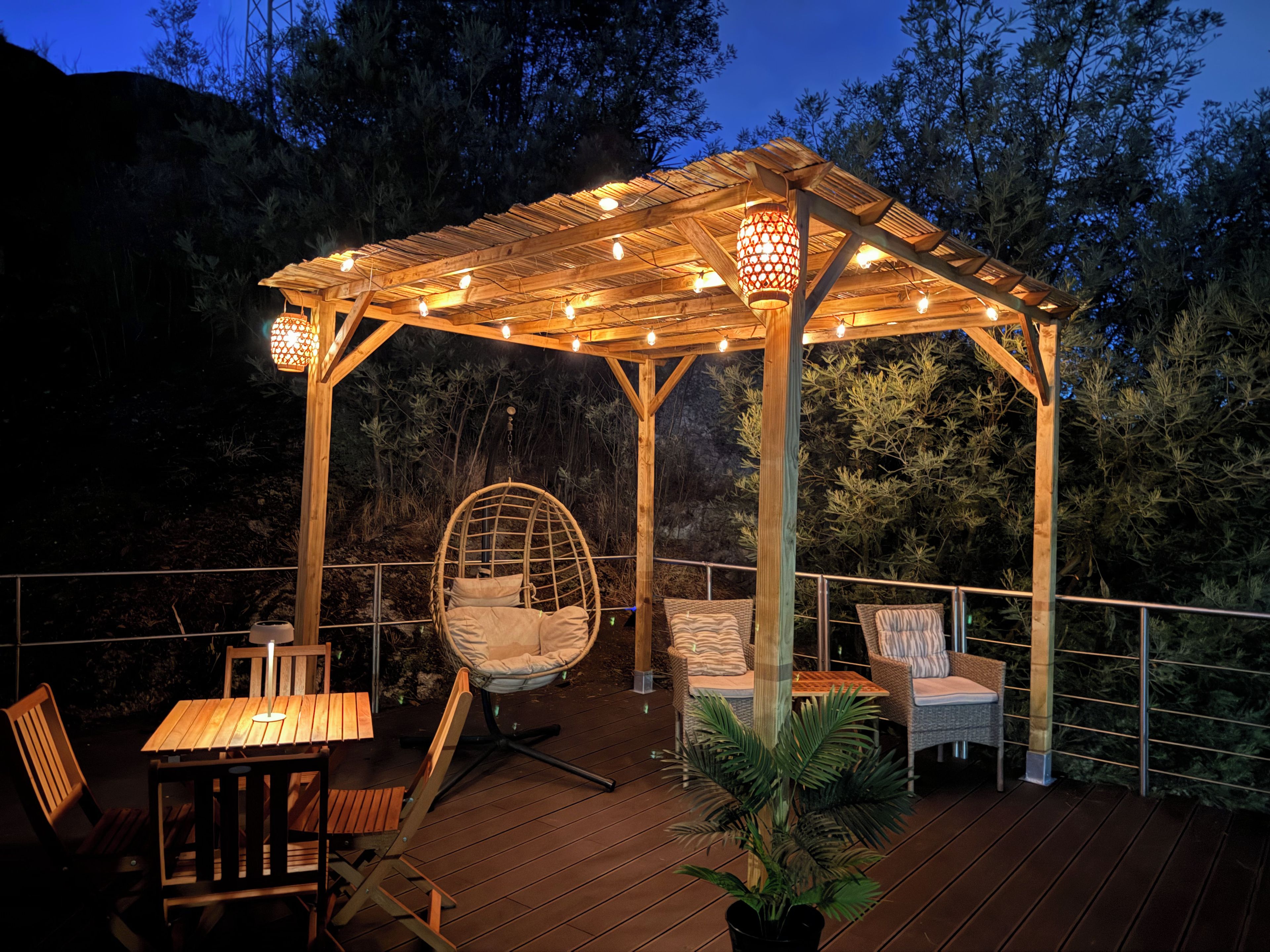 A wooden deck with a pergola, wicker chairs, and a hanging chair.
