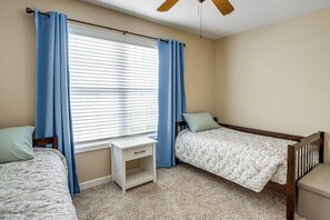 A bedroom with two single beds, a nightstand, a window with blinds, and a ceiling fan. - Screened Porch, Fire Pit! Family Home Near K-State (Manhattan)