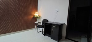 Een kleine kamer met een behang, een bureau met stoel, en een stopcontact.