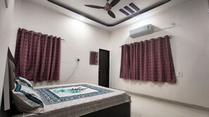 Een slaapkamer met een bed, twee ramen met gordijnen, een plafondventilator, een airconditioning en een deur.