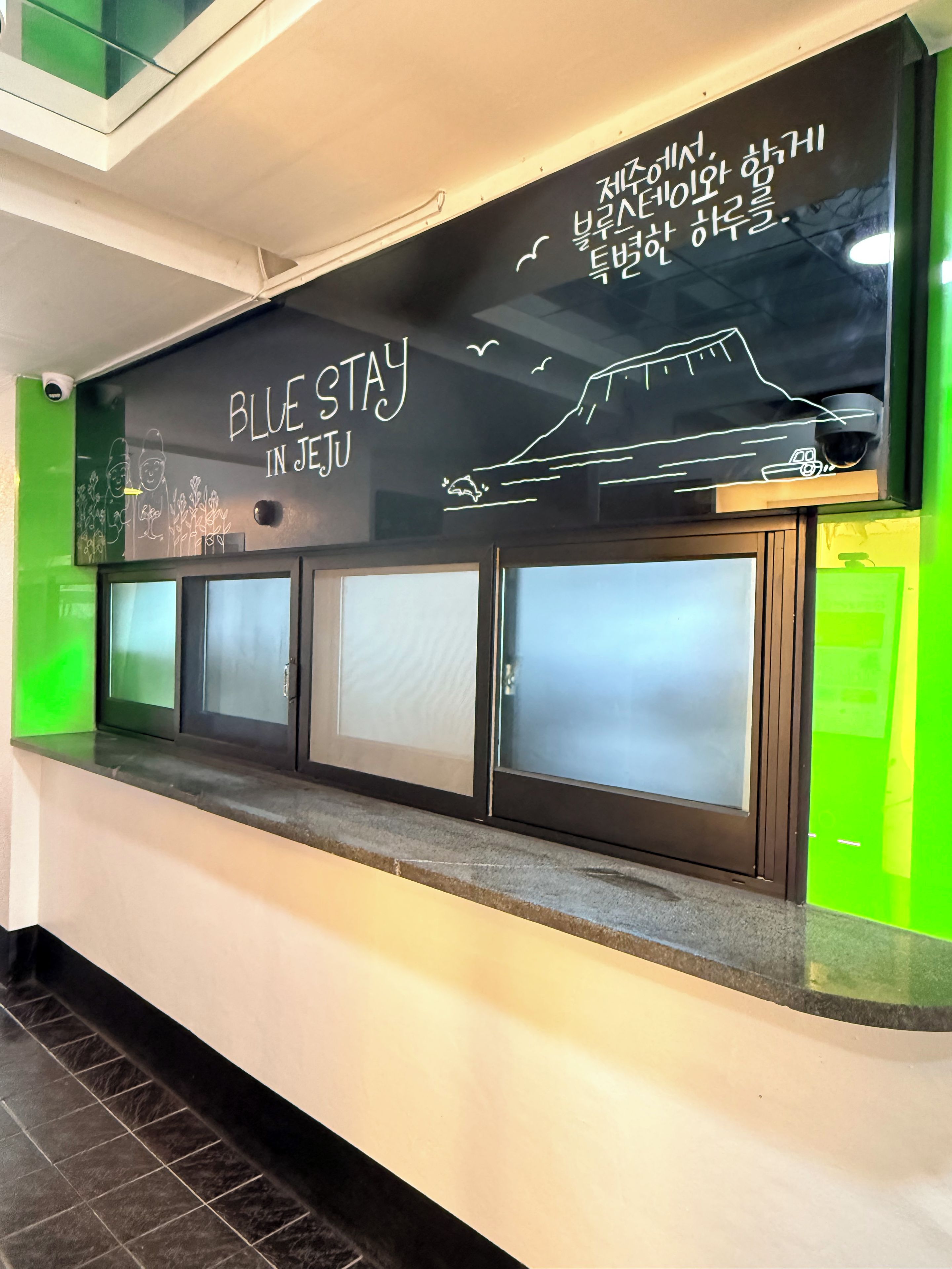 A reception desk with a sign that reads 'BLUE STAY IN JEJU' and a drawing of a ship.
