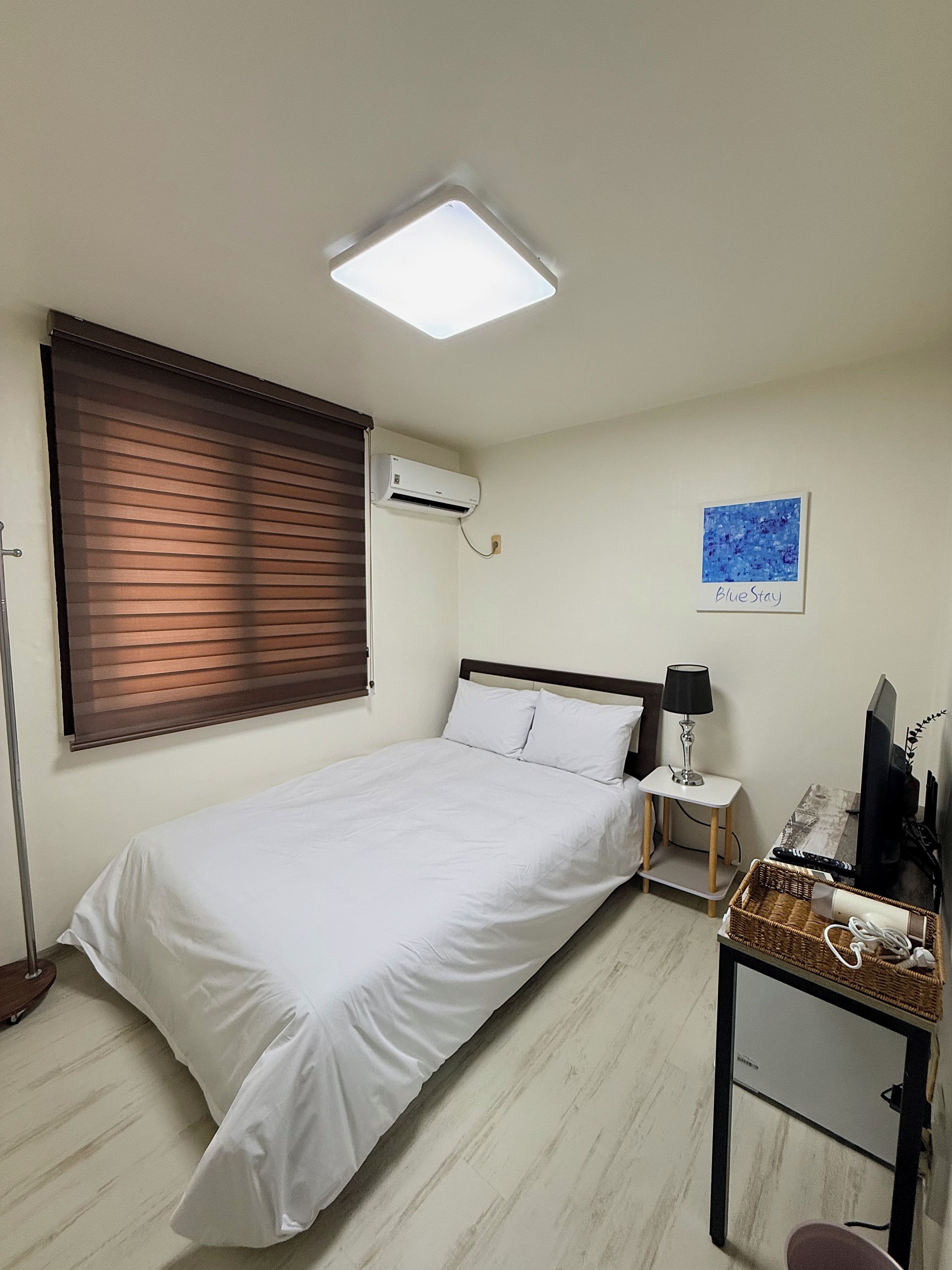 Un dormitorio con cama, mesita de noche, lámpara, televisor y aire acondicionado.