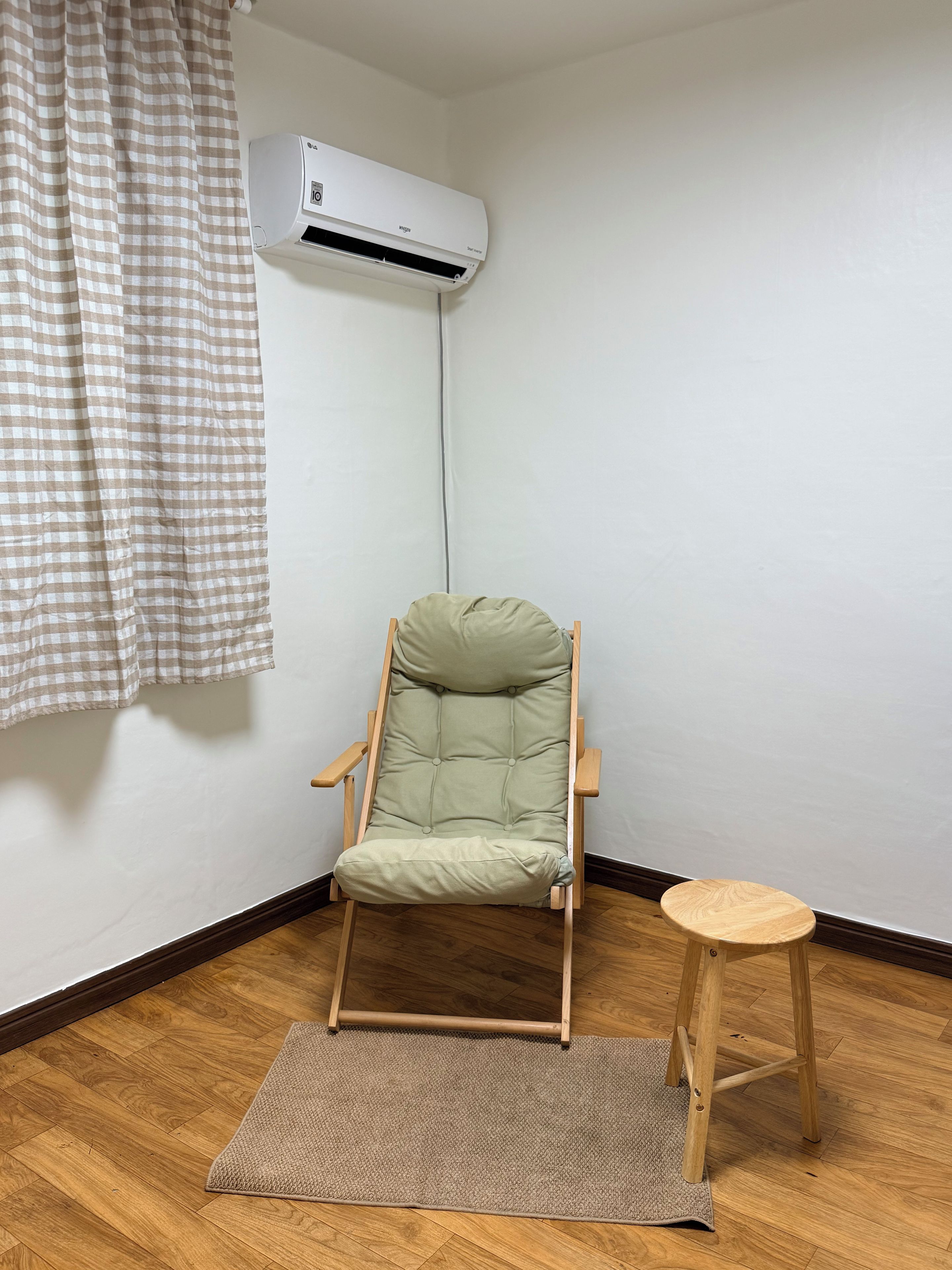 A room with a folding chair, a small wooden stool, a checkered curtain, and an air conditioning unit.