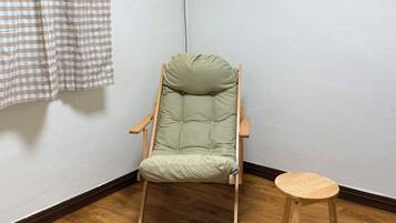 A room with a folding chair, a small wooden stool, a checkered curtain, and an air conditioning unit.