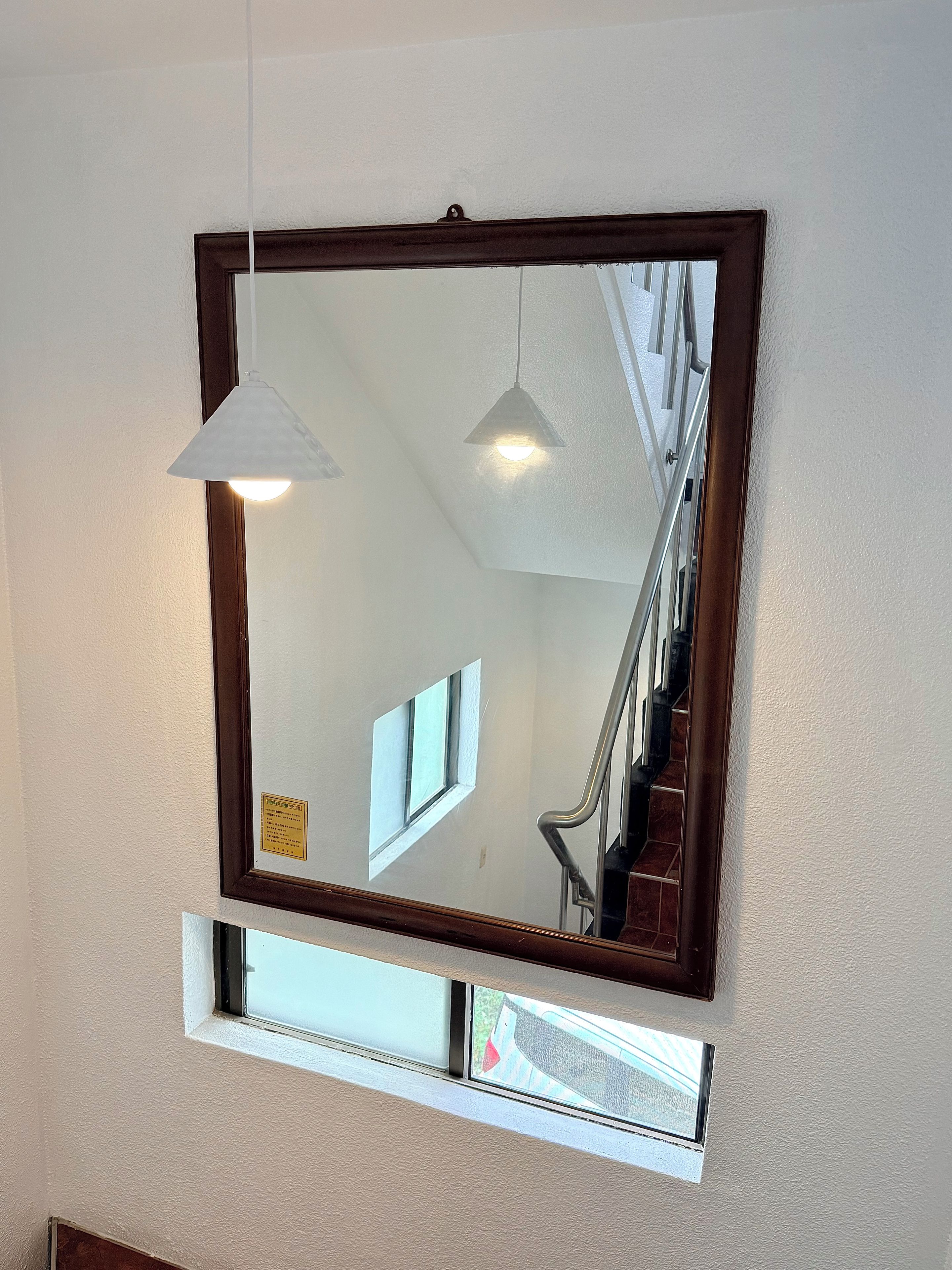 A mirror with a wooden frame, a hanging pendant light, and a window below it.