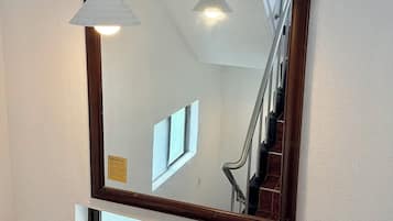 A mirror with a wooden frame, a hanging pendant light, and a window below it.