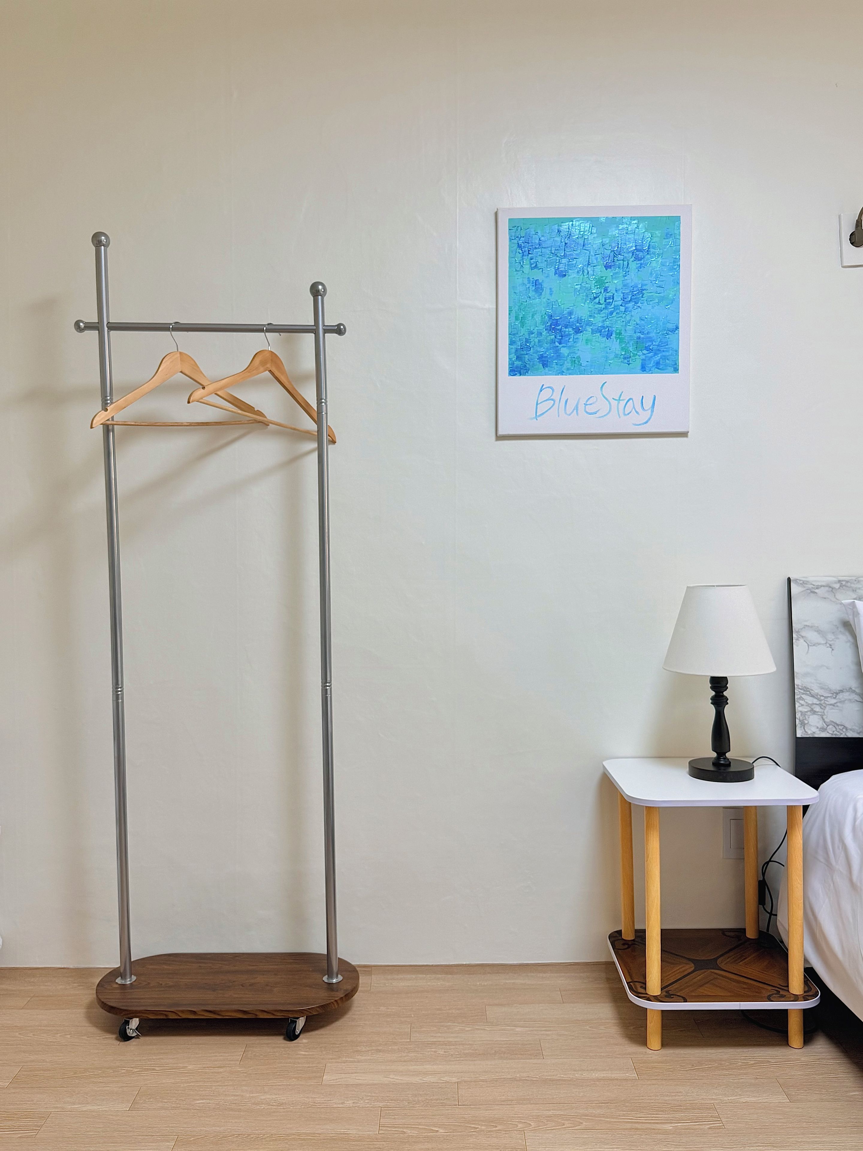 A room with a wooden coat rack, a small table with a lamp, and a framed artwork on the wall.