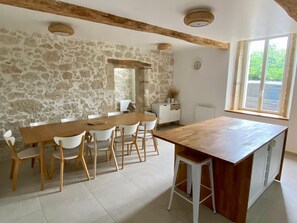 A dining area with a stone wall, wooden ceiling beams, a large table, and white chairs. - Large, air-conditioned villa with a pool, a pétanque court, and a garden. (Castelculier)