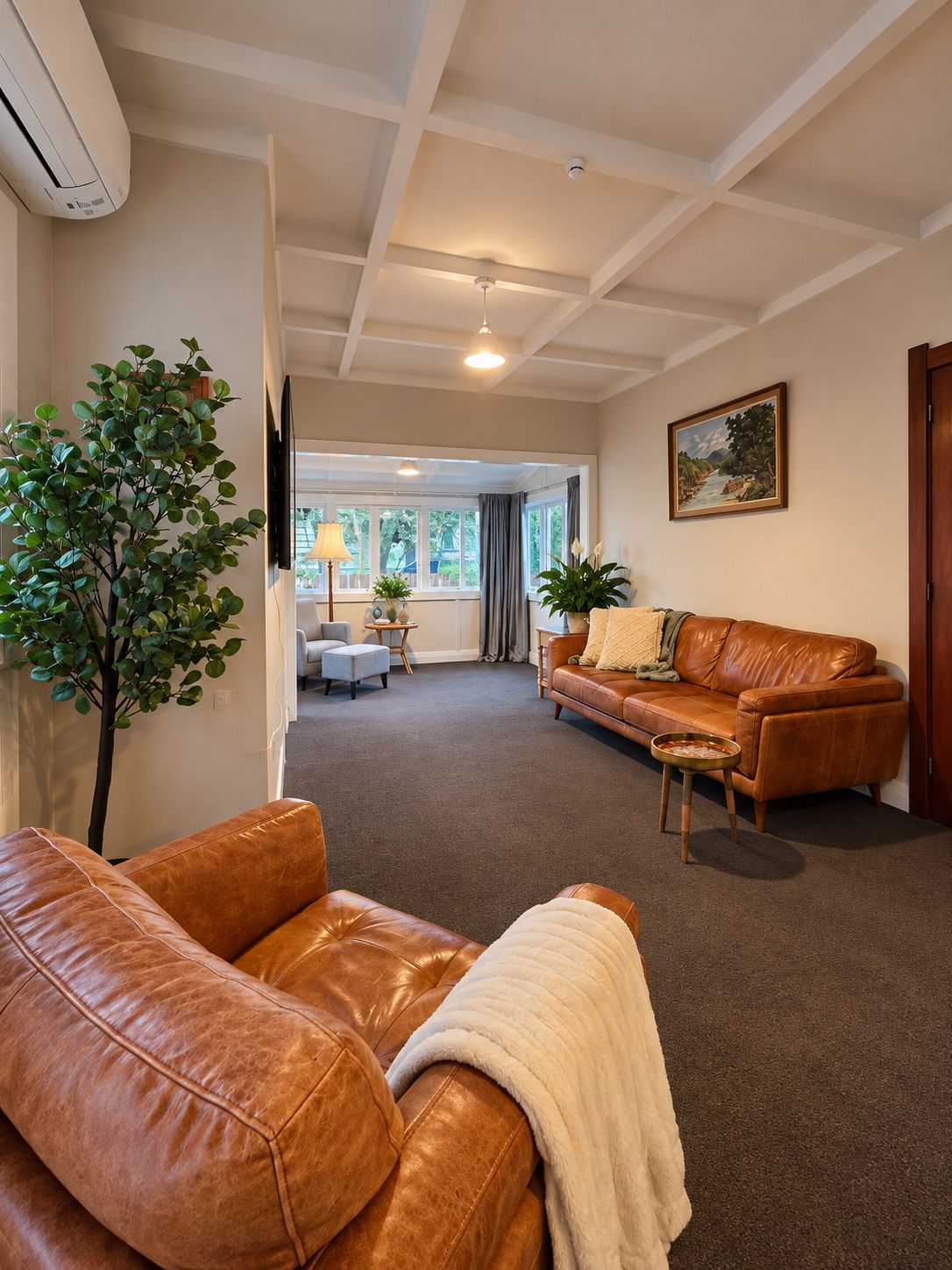A living room with a brown leather sofa, a coffee table, a plant, and a painting on the wall.