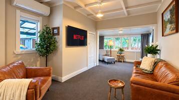 Ein Wohnzimmer mit Ledersofas, einem an der Wand befestigten Fernseher und einem Deckenventilator.