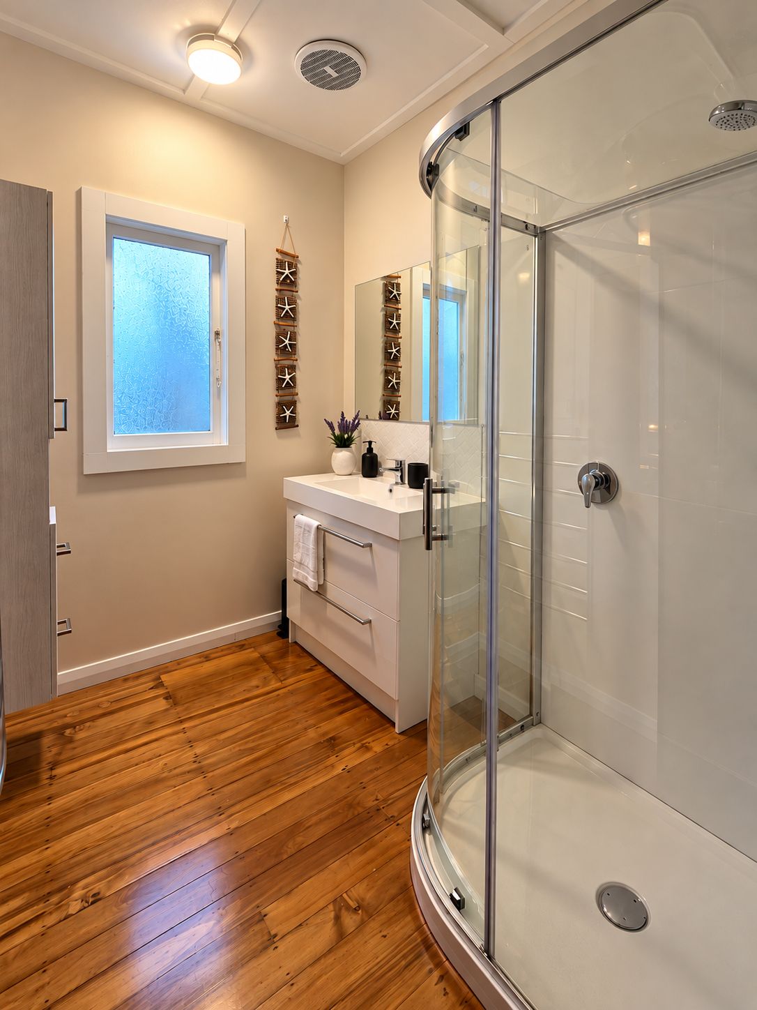 Bright modern bathroom with glass shower and warm wood-style floors
