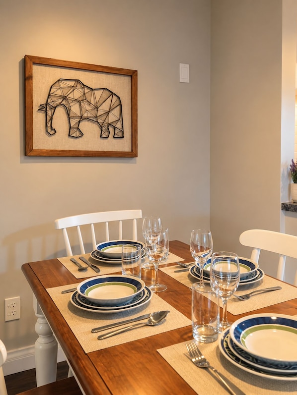 Een gedekte eettafel met borden, glazen en bestek, met een lijstwerk met abstracte dierenkunst aan de muur.