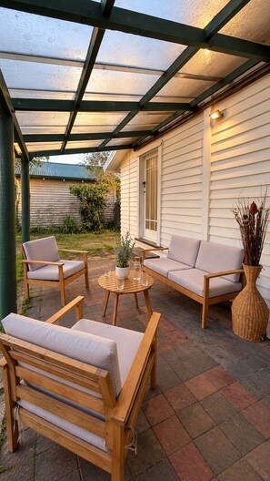 Een overdekt terras met een houten bank, een sofa en een tafel.