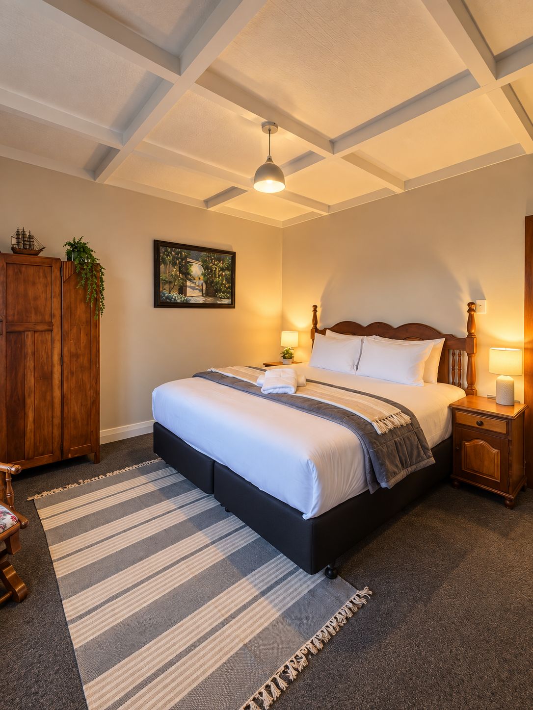 Ein Schlafzimmer mit einem großen Bett, einem Holzkopfende, Nachttischlampen, einem gerahmten Bild an der Wand und einem Holzschrank.