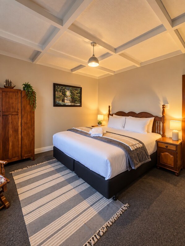 A bedroom with a large bed, wooden headboard, bedside lamps, a framed picture on the wall, and a wooden wardrobe.