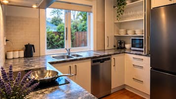 A modern kitchen with a stainless steel refrigerator, a dishwasher, and a sink. There is a window providing a view of the outdoors.