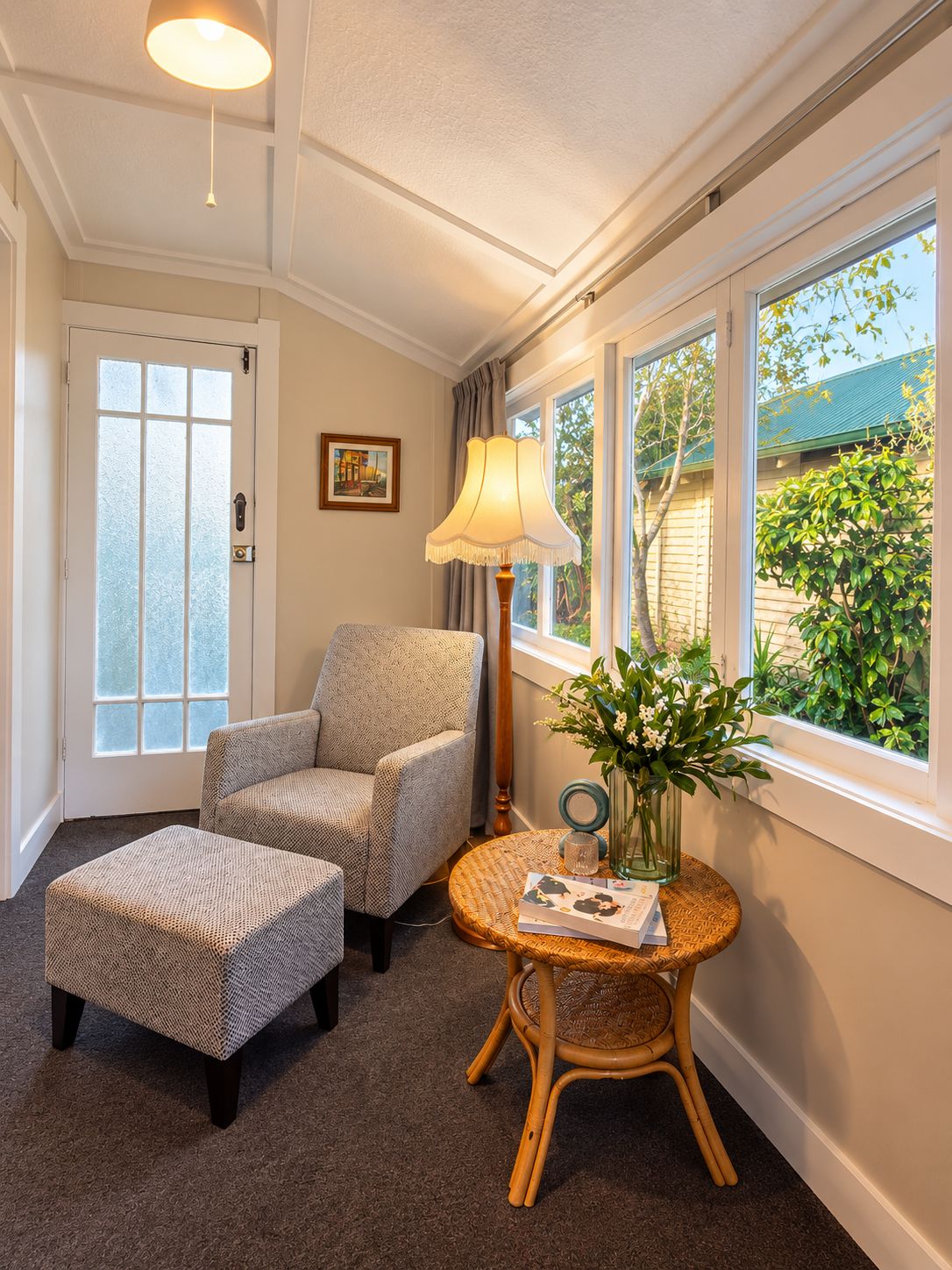 A room with a door, two armchairs, a small table with a vase, and a lamp.