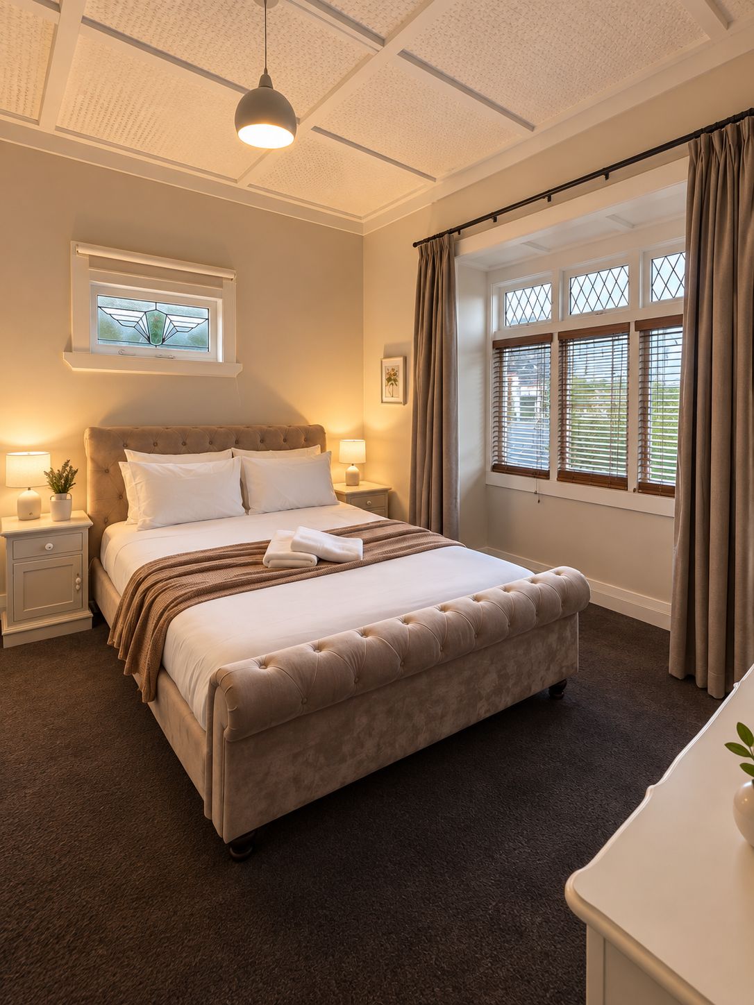 A bedroom with a large bed, bedside tables, a window with curtains, and a ceiling light.