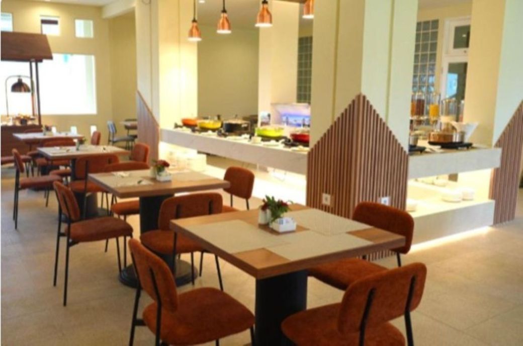 Ein Restaurant mit Tischen, Stühlen und einer Theke mit Lebensmitteln, beleuchtet durch Pendelleuchten.