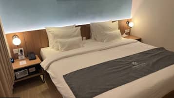 Quarto de hotel com cama, abajures, mesa de cabeceira e luminária na parede.