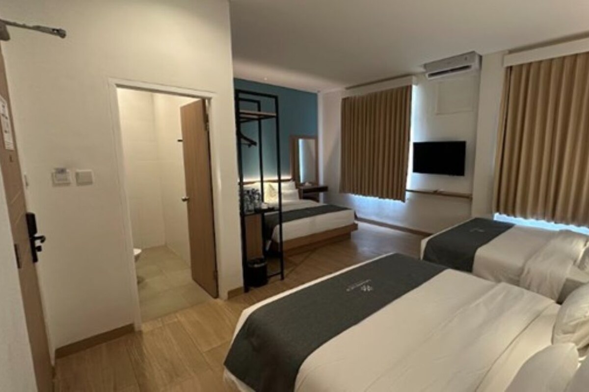 A hotel room with two beds, a TV, a desk, and a window with curtains.