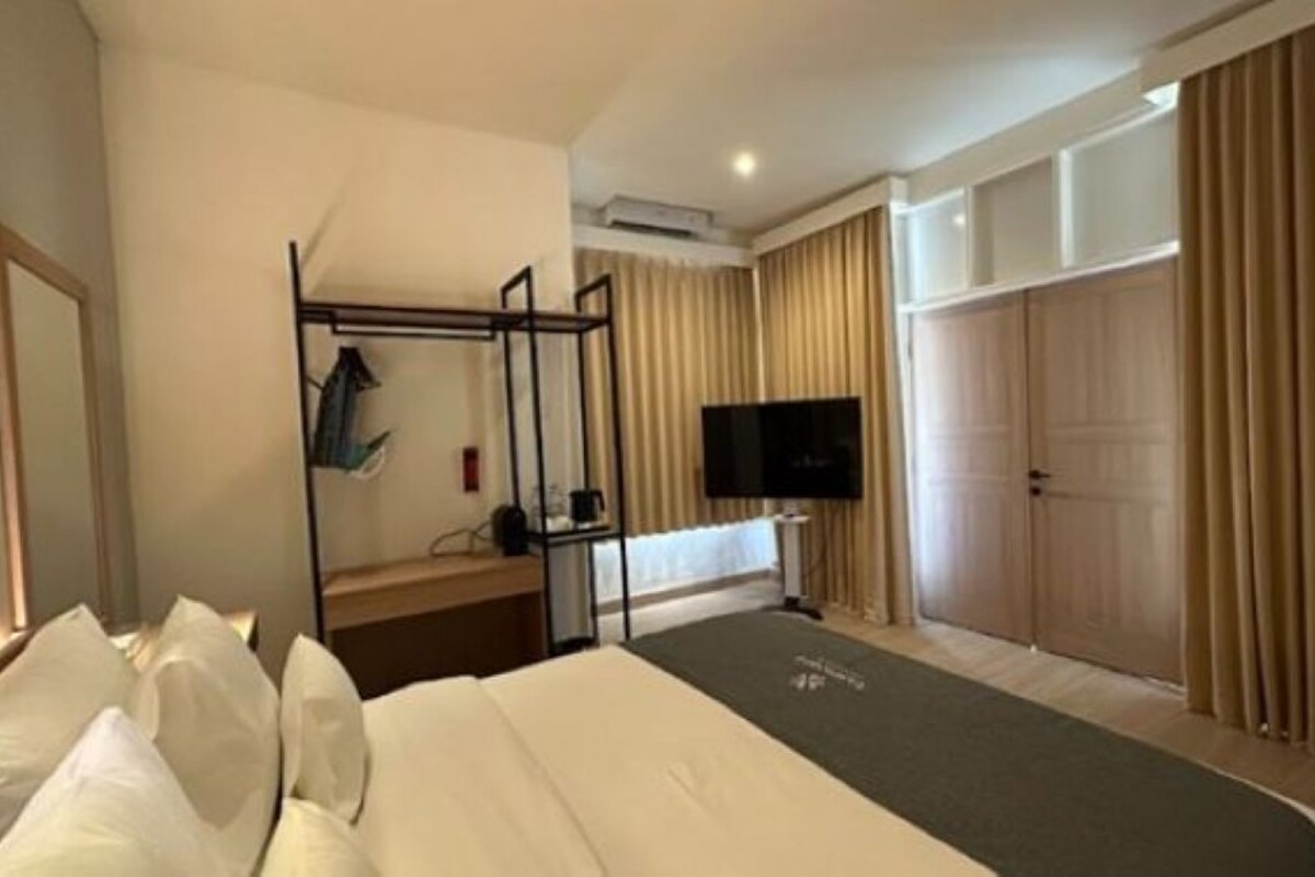 A hotel room with a bed, a desk with a chair, a television, and a wardrobe.
