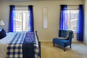 Ein Schlafzimmer mit einem Bett, einem Sessel und zwei vorhängeverzierten Fenstern.